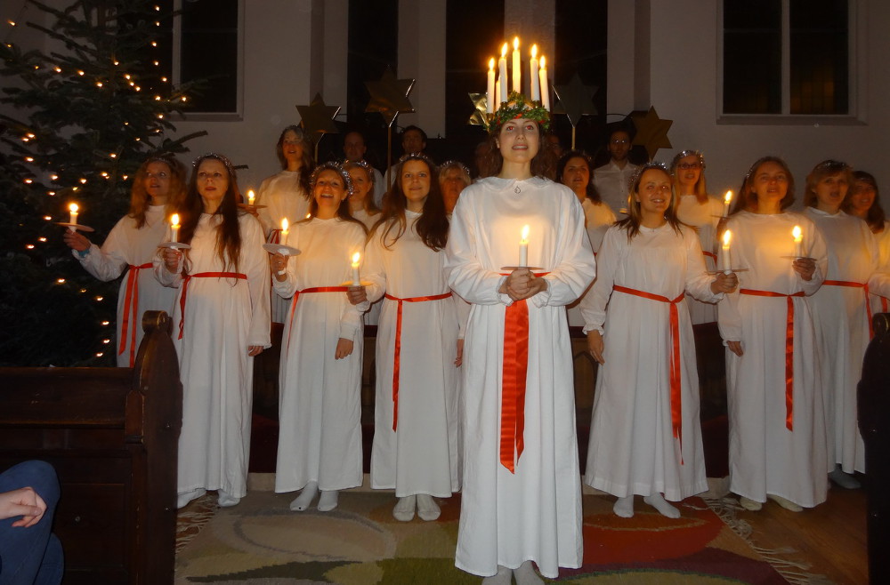Die Lucia trägt einen Kerzenkranz auf dem Kopf, die anderen Frauen halten eine Kerze in der Hand.