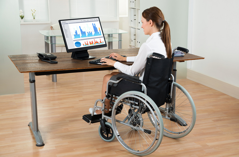Young Businesswoman On Wheelchair Analyzing Graph On Computer In Office