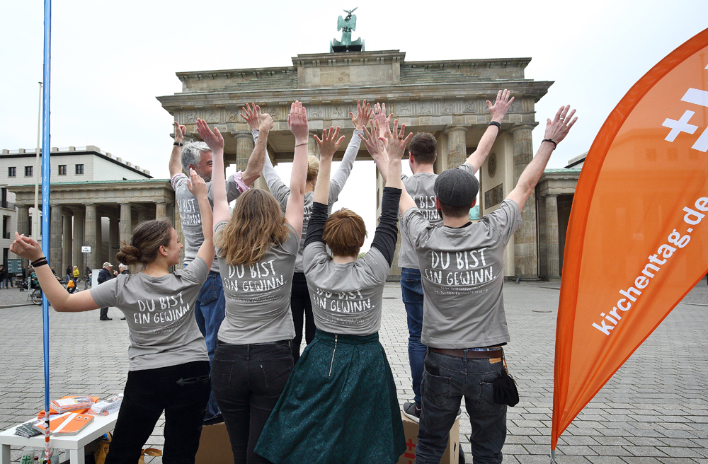 Mit Blick auf das Brandenburger Tor: Helfer präsentieren ihre Shirts für den Kirchentag