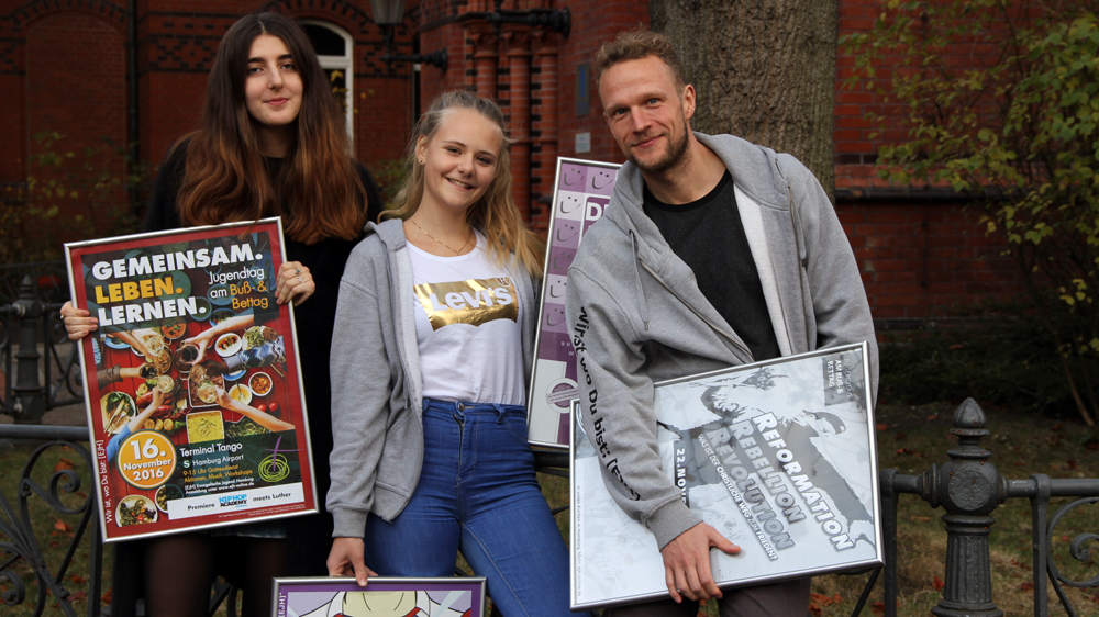 Die EJH-Vorstandsmitglieder Jelena Pohl (19) und Leah Hamann (18) sowie Bildungsreferent David Barth (v.l.) mit Plakaten von verschiedenen Jugendtagen