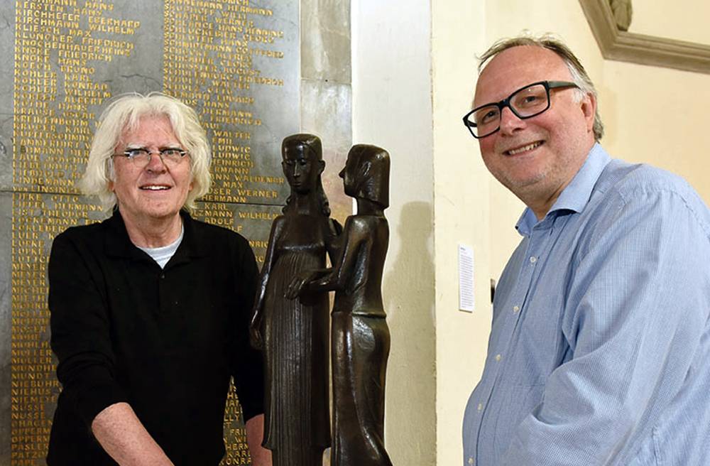 Kurator Peter Rautmann (li.) und Pastor Betram Sauppe platzieren die Skulptur "Social conciousness" vor der Gefallenen-Gedenktafel