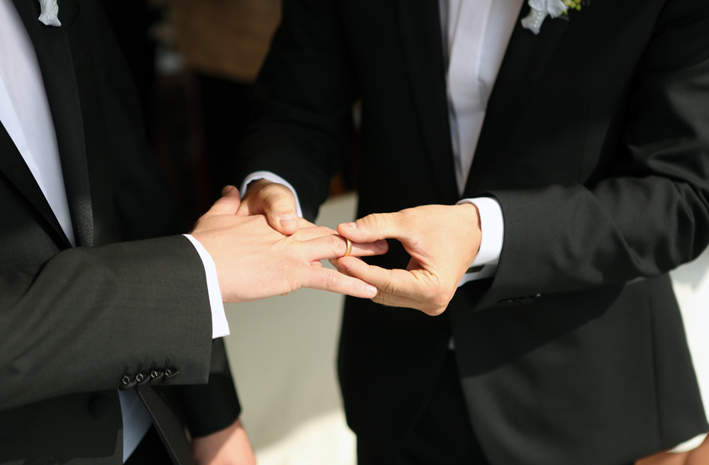 Zwei Männer im Hochzeitsanzug stecken sich gegenseitig die Ringe an