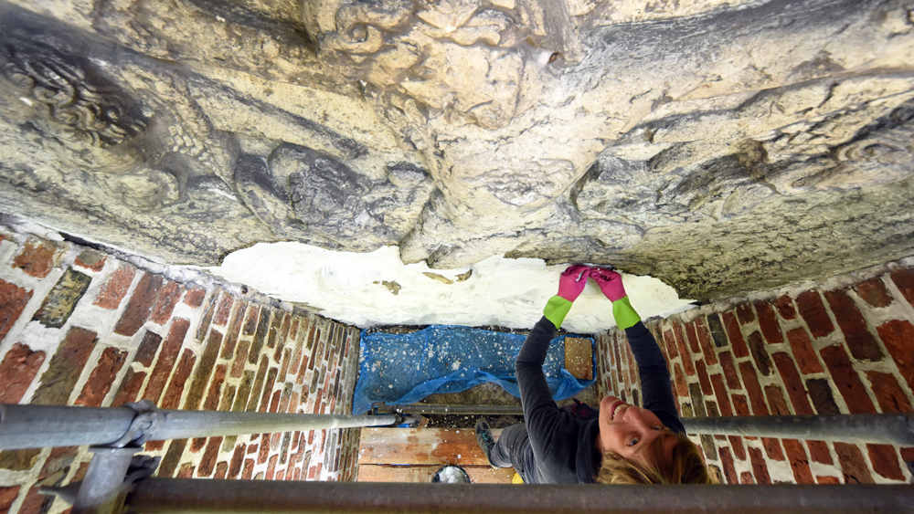 Restauratorin Malaika Krohn am Steinrelief von Jesus am Kreuz