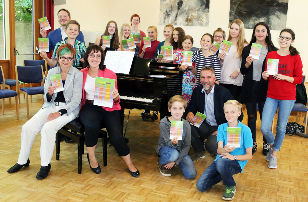Bischof Jan Janssen (hockend) und Landeskirchenmusikdirektorin Beate Besser (sitzend, links) präsentieren gemeinsam mit dem Jugendchor von Birgit Wendt-Thorne (sitzend, rechts) das neue Liederheft
