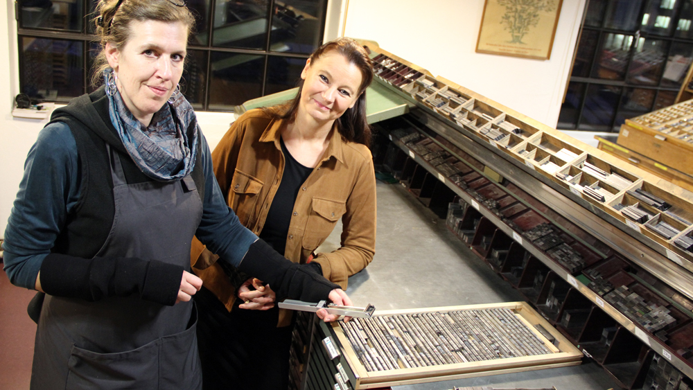 Anne von Karstedt (l.), Werkstätten-Leiterin im Museum der Arbeit, und Lektorin Astrid Froese an einer historischen Druckmaschine
