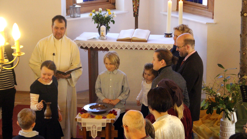 Mattis Brandt wird von Pastor Torsten Kiefer getauft, Kinder füllen das Taufbecken mit Wasser