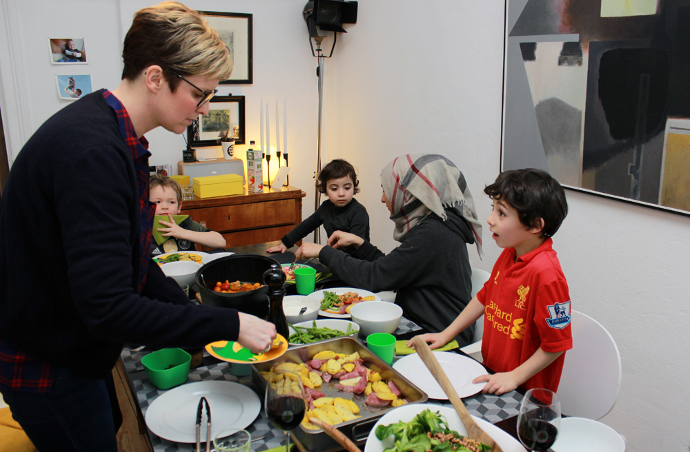 Karim (re.) freut sich sichtlich auf Rosmarinkartoffeln und Salat, die Gastgeberin Judith Fietz auffüllt. Karims Mutter Rasal schneidet das Fleisch für Tochter Lana.
