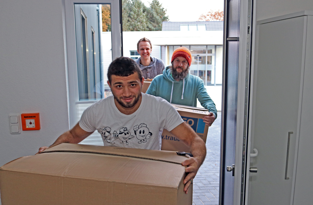 Einzug (v.l.): Abdul, Til Waschek und Ole Martens tragen die Kartons ins Wohnhaus