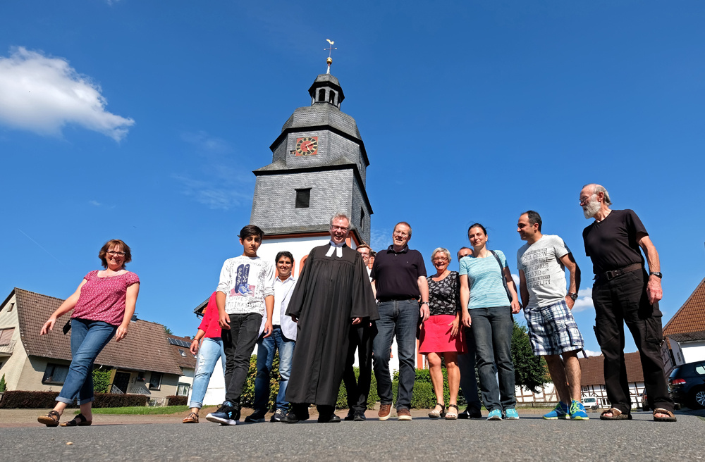 Pastor Jens-Arne Edelmann mit Dorfbewohnern und Flüchtlingen vor der St. Marienkirche in Wollershausen