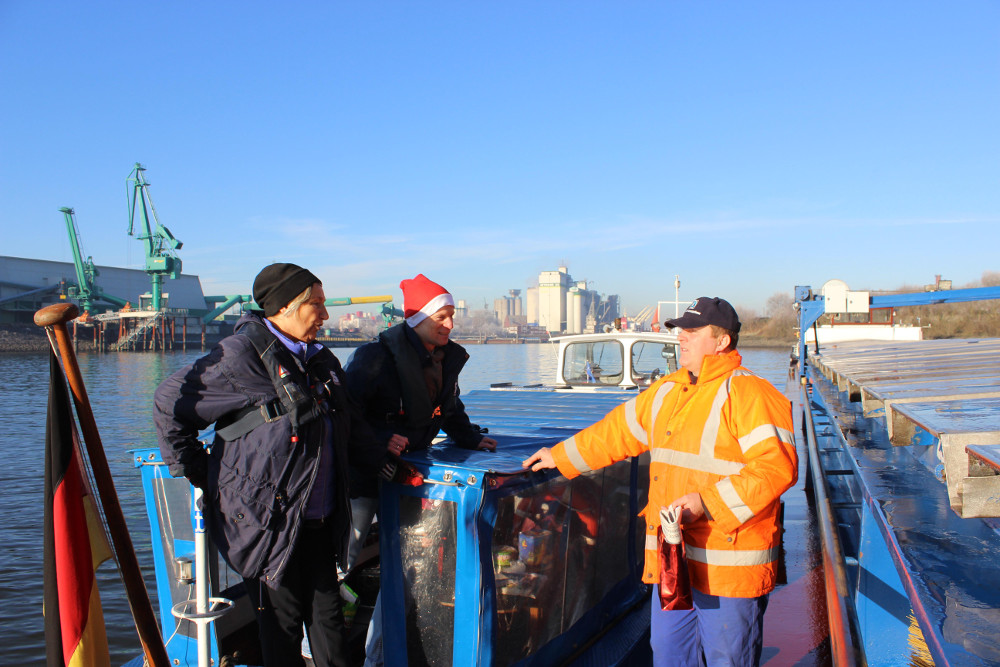 Christel Zeidler und Seemannspastor Matthias Ristau überreichen zu Nikolaus einen süßen Gruß an Binnenschiffer Darius Giergowski (rechts) im Hamburger Hafen.