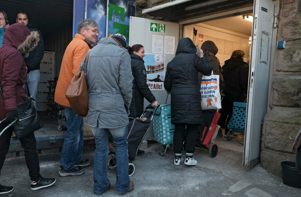 Bedürftige warten vor einer Tafel auf die Ausgabe von Lebensmitteln.