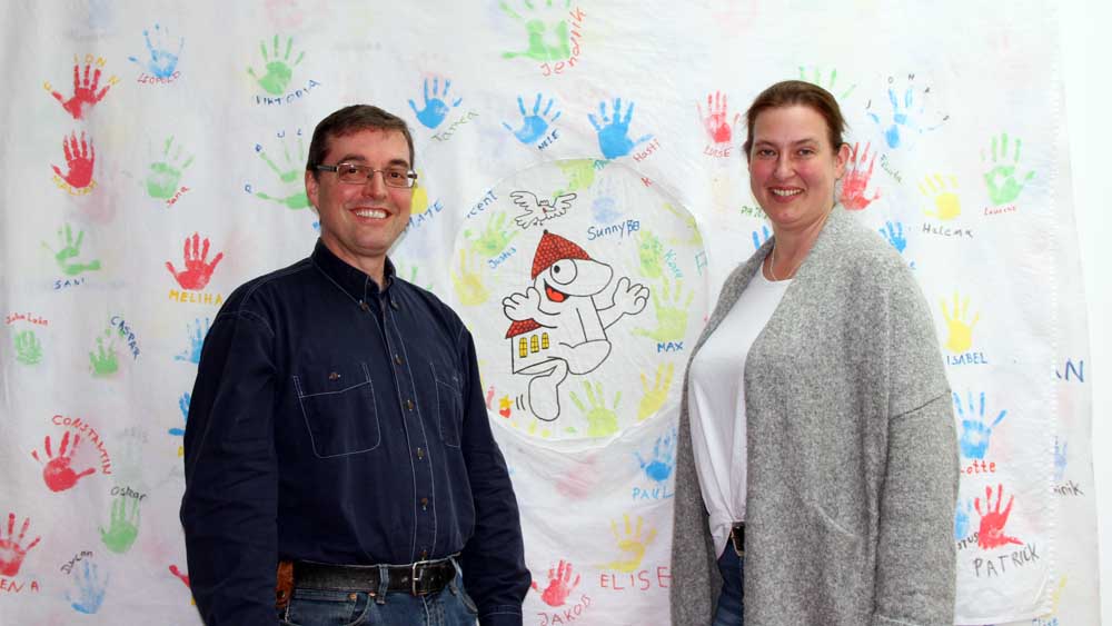 Pastor Hago Michaelis und die ehrenamtliche Helferin Anja Brunnemann vor Handabdrücken von Kindern und Eltern