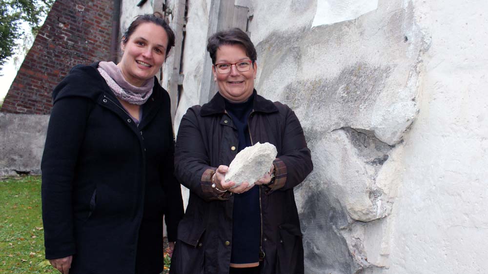 Die Pastorinnen Pastorin Annett Weinbrenner (li.) und Ulrike Egener zeigen vor der Kirche auf zerbeulte Steine aus dem Mauerwerk