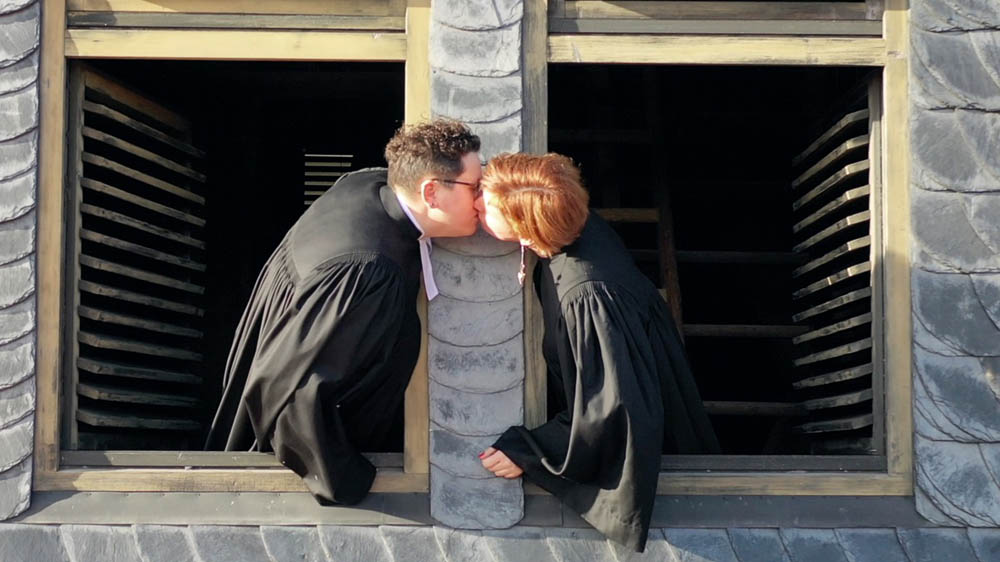 Zwei Frauen im Talar küssen sich am Fenster eines Kirchturms