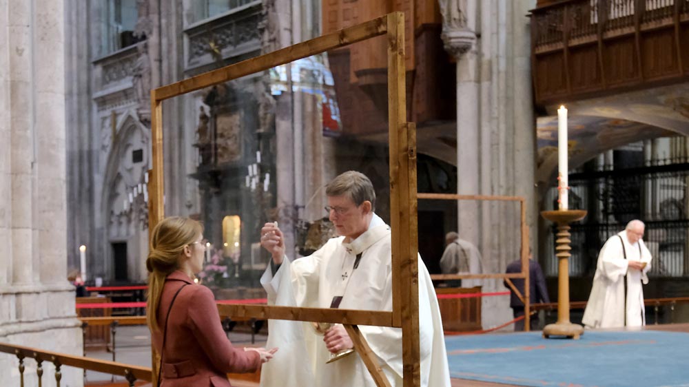 Erzbischof Woelki teilt hinter einer Scheibe die Kommunion aus