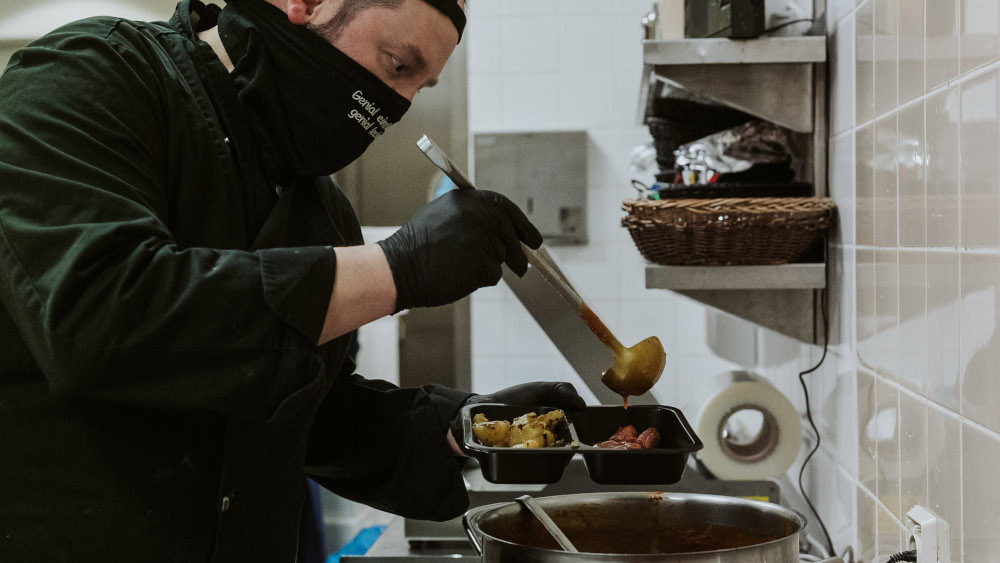 Der Koch Christopher Winkler vom Caterer „Guthaben – Kantinen und Catering“ füllt Teller mit warmen Mahlzeiten.