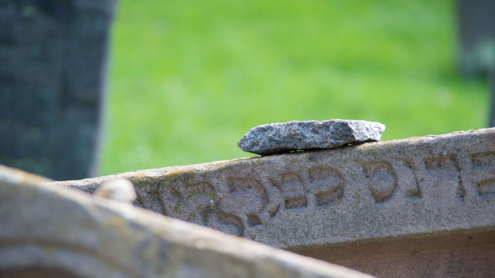 Jüdischer Grabstein mit abgelegtem Stein eines Besuchers.