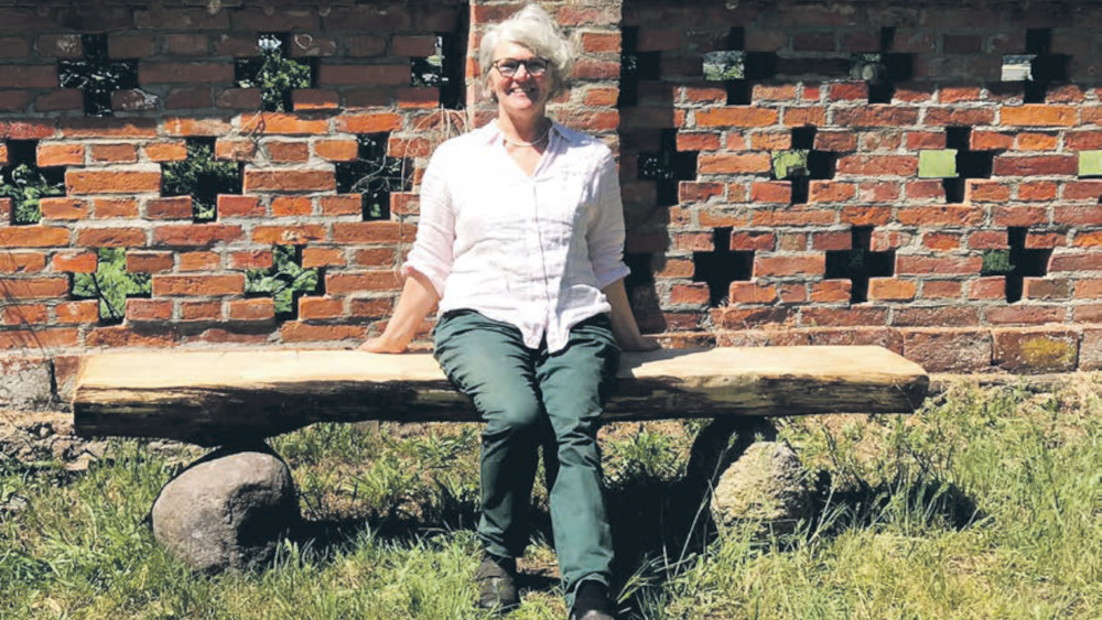 Pastorin Gesine Isbarn testet eine der vier Bänke aus Eiche und Feldsteinen, die jetzt rund um die Varchentiner Kirche und auf dem dortigen Friedhof zu finden sind. 