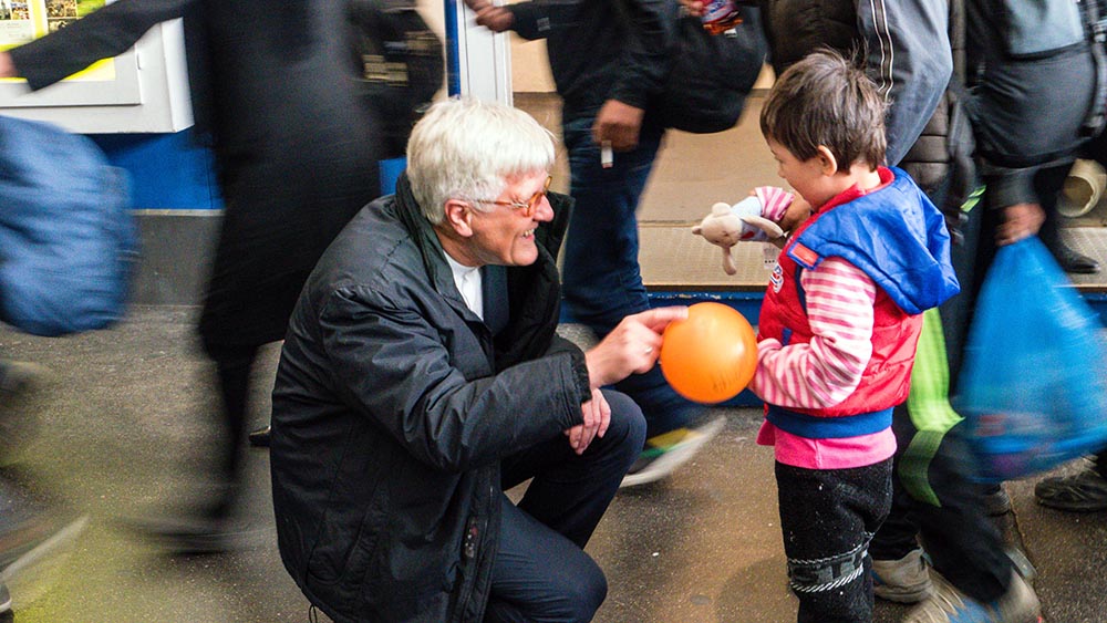Heinrich Bedford-Strohm im September 2015 am Bahnhof München mit einem Flüchtlingskind