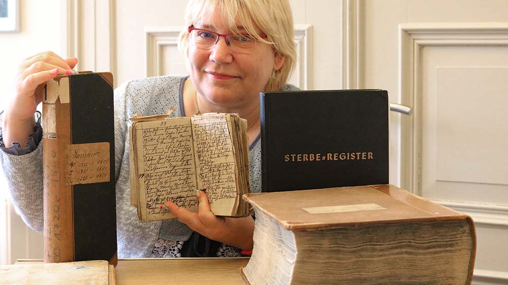 Jana Holzberg mit antiken Büchern, auf einem steht „Sterberegister“