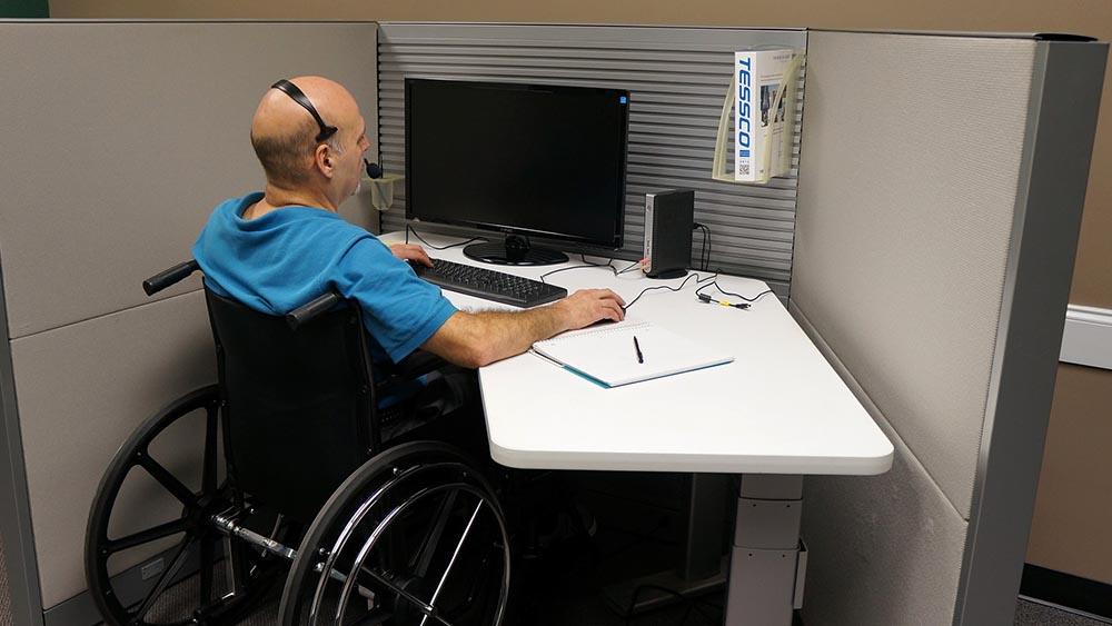 Mann im Rollstuhl sitzt im Büro an einem Computer