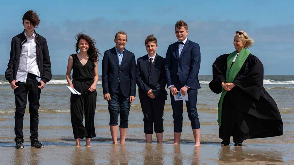 Mit den Füßen stehen die Konfirmanden und Pastorin Constanze Lange in der Nordsee