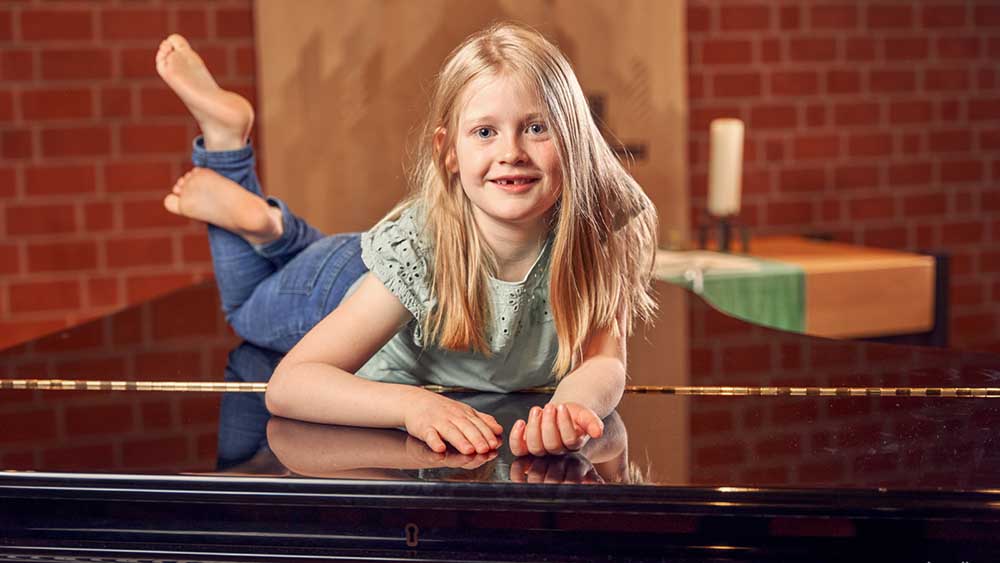 Ein Mädchen des Kinderchors hat sich für das Foto auf den Flügel gelegt