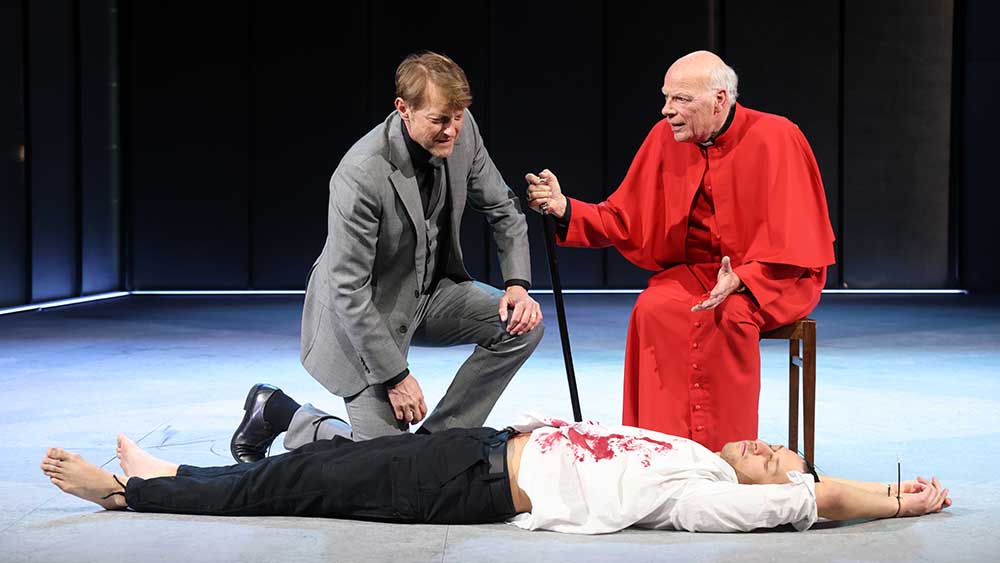 Der Großinquisitor (Gerhard Ulrich) diskutiert mit König Phillipp II (Imanuel Humm). Den Tod des Marquis von Posa (Calvin-Noel Auer) ignoriert der Kirchenmann.