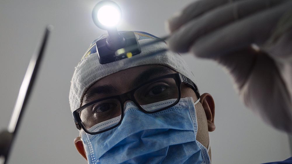 Arzt mit Maske und Pinzette, von unten ins Gesicht fotografiert