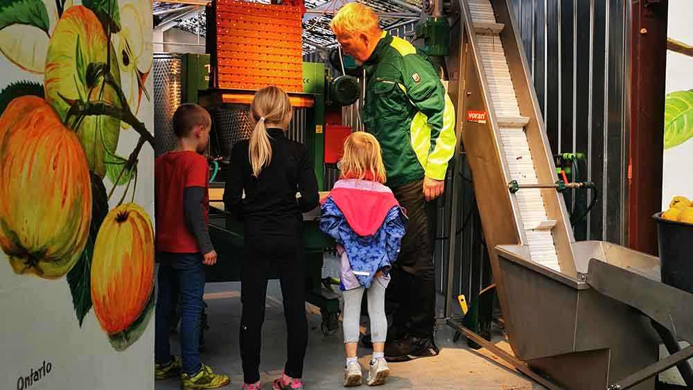 „Wie funktioniert denn das?“ David, Finja und Nele lassen sich von Christian Uhlemann die Mostmaschine erklären