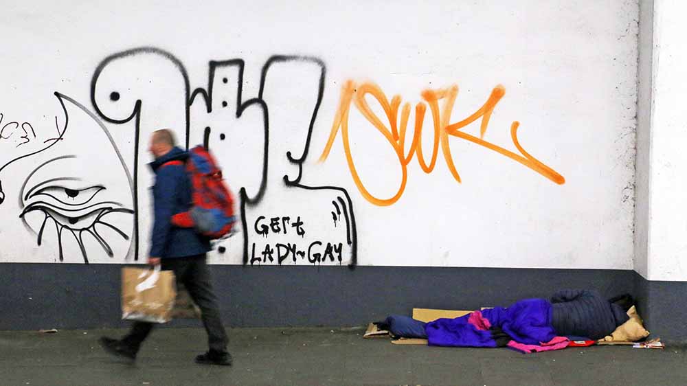 Unbeachtet von Passanten liegt ein Odachloser am Straßenrand Foto: Dieter Sell / epd