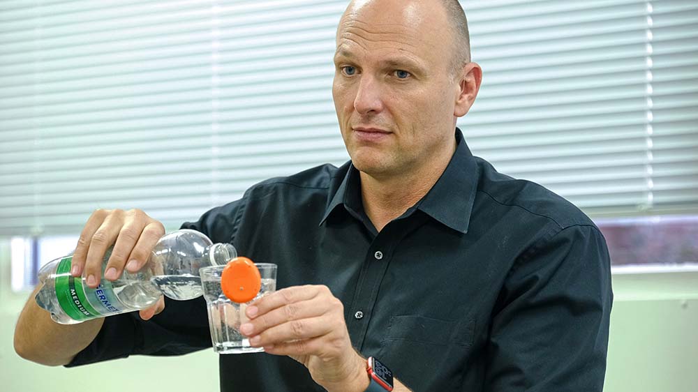 Marcell Feldmann gießt sich Wasser ein. Die Vorrichtung am Glas vibriert, wenn das Glas voll ist