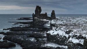 zum Teil von Schnee bedeckte Felsen, die ins Meer ragen, an der isländischen Küste