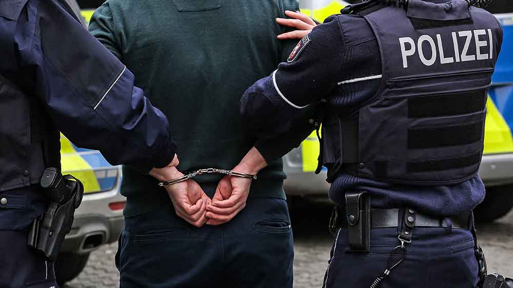 Mann mit gefesselten Händen hinter dem Rücken, zwei Polizisten führen ihn ab