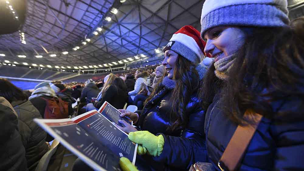 Zwei Frauen mit Weihnachtsmann-Mütze sitzen im Stadion und singen