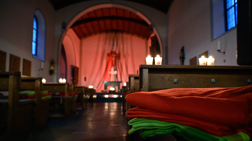 Fleecedecke und Kerzen liegen auf einer Kirchenbank in einer Dorfkirche in Oberjosbach bei Niedernhausen.