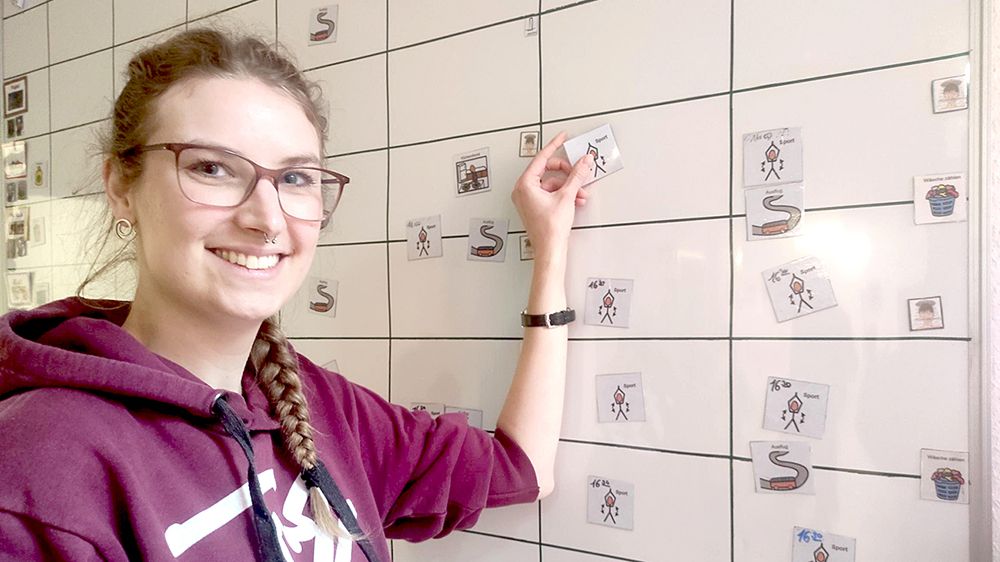 Judith Jansen am Wochenplan im JuLe1-Haus. Symbole zeigen den Jungen und Mädchen, welche Aktion oder welcher Termin am jeweiligen Tag ansteht.