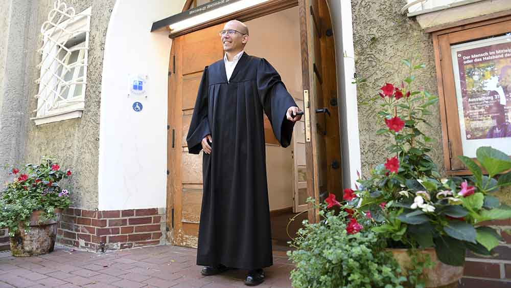 Mann mit Talar steht am Eingang einer Kirche
