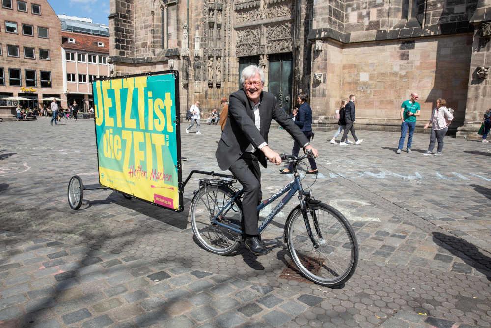 Landesbischof Heinrich Bedford-Strohm präsentiert die Kampagne des Kirchentages auf dem Fahrrad vor der Lorenzkirche in Nürnberg