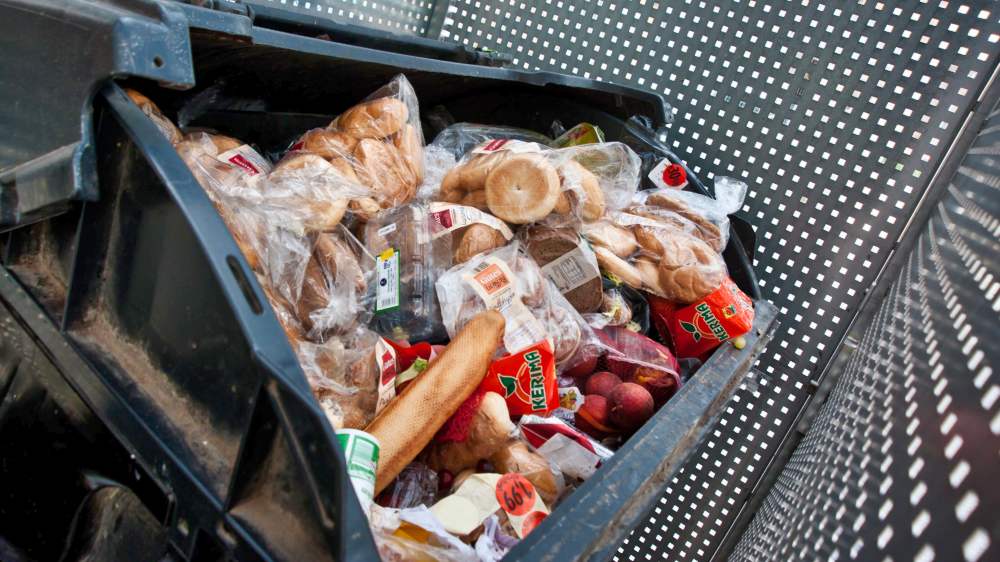 Teilweise noch verpackte Lebensmittel in einer großen schwarzen Mülltonne