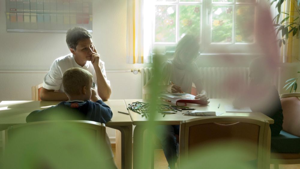 3 Kinder sitzen it einer Betreuerin an einem Tisch