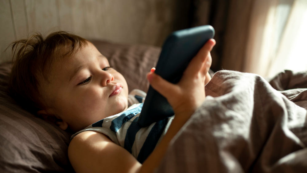 Kleinkind mit Smartphone im Bett