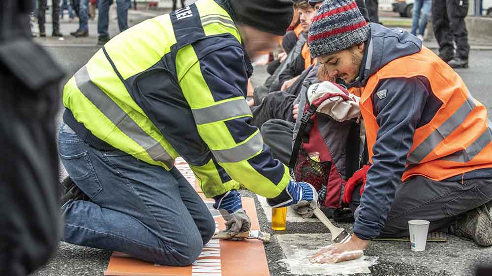 Zwei Aktivisten in Warnwesten, Polizist löst den Kleber