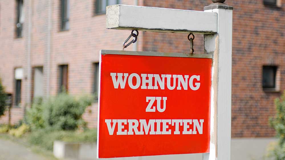 Rotes Schild mit der Aufschrift "Wohnung zu vermieten" vor einem Wohnhaus