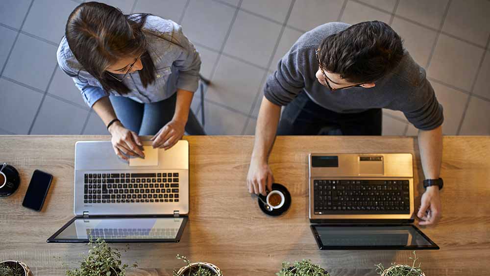 Mann und Frau sitzen vor Notebook, von oben fotografiert