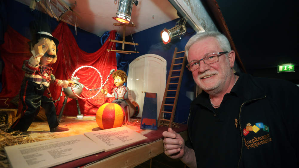 Im Augsburger Puppenspielmuseum "Die Kiste" steht Puppenkisten-Chef Klaus Marschall neben der Vitrine mit der Roboter- Marionette "Schlupp vom grünen Stern"