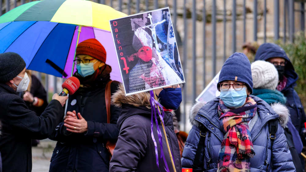 Missbrauchsbetroffene und Vertreterinnen verschiedener Kircheninitiativen stehen mit Plakaten vor der Residenz des Essener Bischofs.