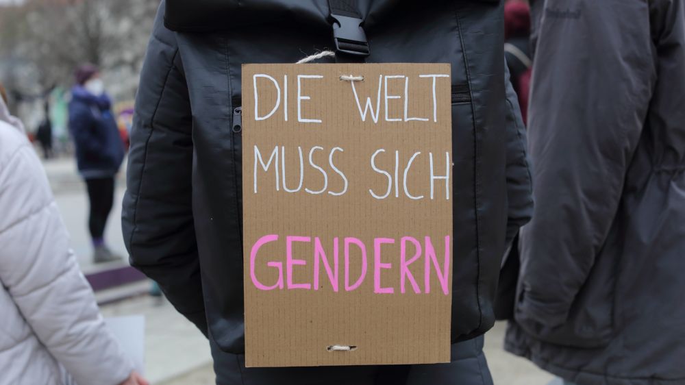 Auf einem Rucksack hängt ein Schild mit der Aufschrift "Die Welt muss sich gendern"