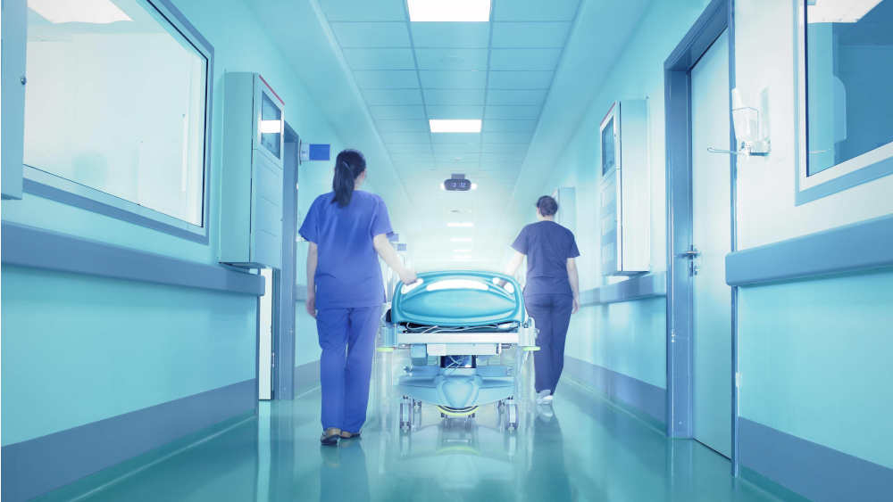 Zwei Krankenschwestern schieben ein Bett durch den Flur eines Krankenhauses