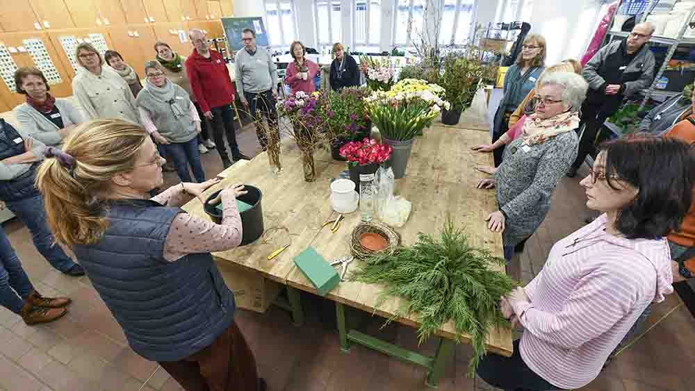 Menschen stehen um einen großen Tische herum, auf dem viele Blumen lagern